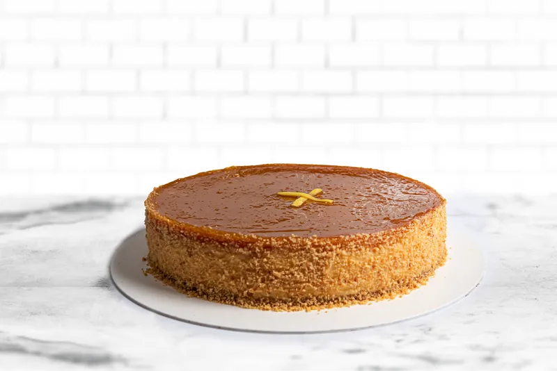 Cheesecake horneado entero de Boston Bakery sobre base de mármol con pared de azulejo blanco