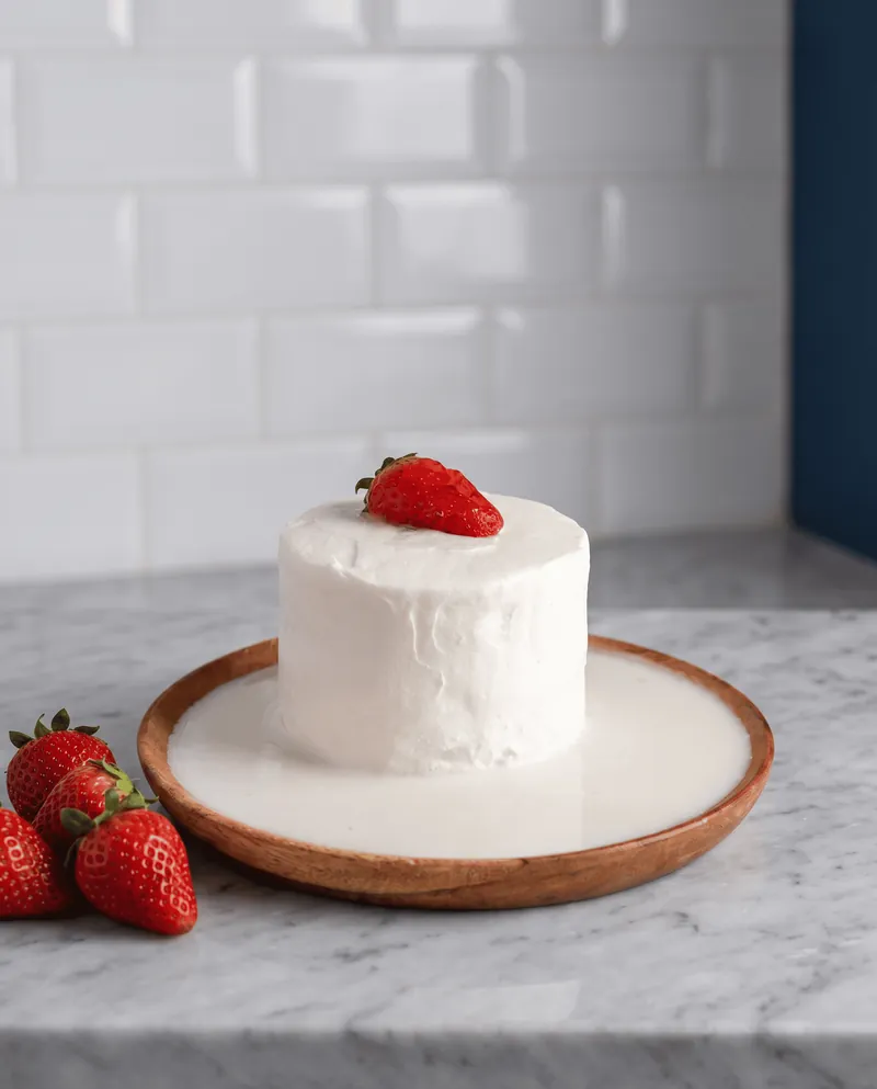 Pastel de tres leches entero con fresa sobre base de madera y mármol