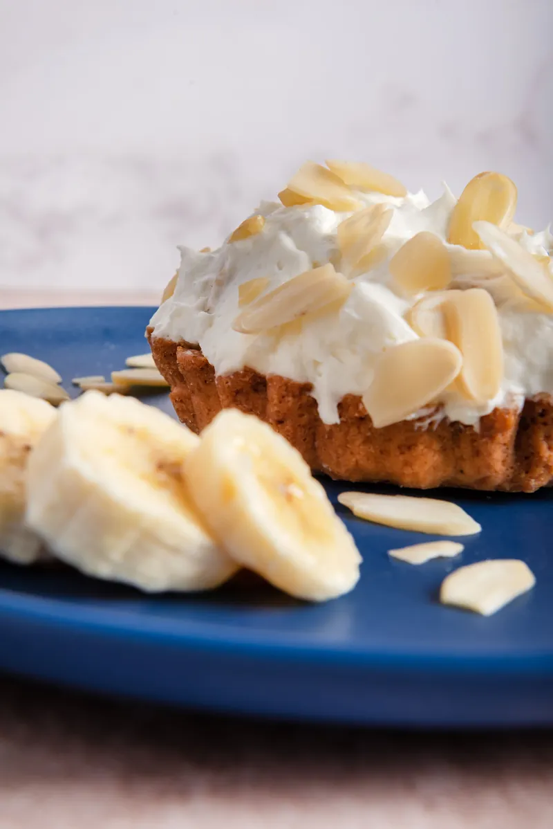 Tarta individual de plátano con crema batida y almendra fileteada en plato azul