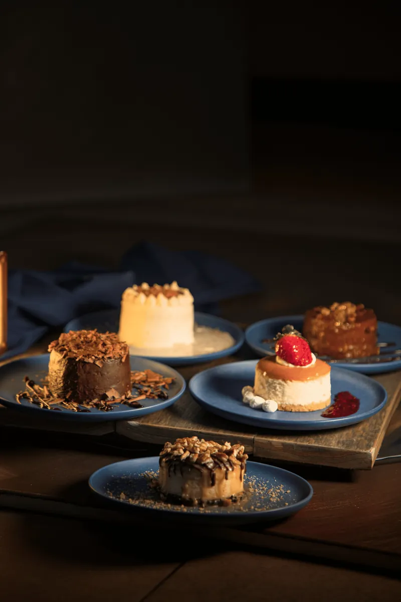 Bodegón de postres individuales surtidos de Boston Bakery en platos azules con iluminación cálida