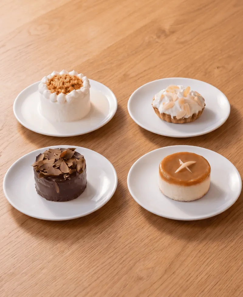 Cuatro postres individuales de Boston Bakery en platos blancos sobre mesa de madera