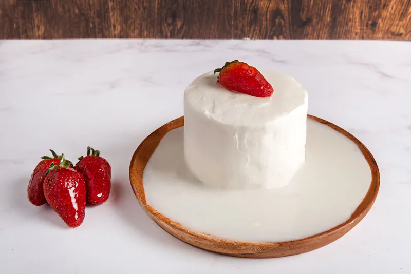 Pastel de tres leches individual con fresa sobre tabla de madera y fresas frescas al lado