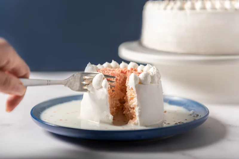 Pastel de tres leches individual siendo cortado con tenedor sobre plato azul de Boston Bakery