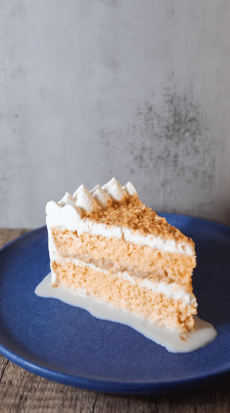 Rebanada de pastel de tres leches con crema sobre plato azul