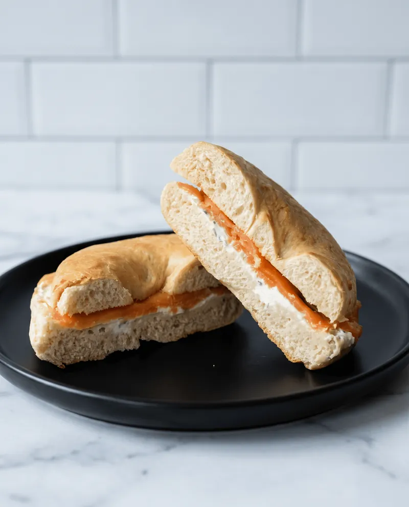 Bagel con salmón partido a la mitad servido en plato negro sobre mármol