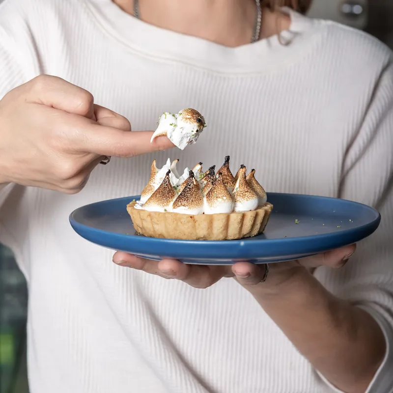 Persona sosteniendo un plato azul con tarta individual de limón y merengue flameado