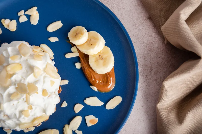 Detalle de crema batida, rodajas de plátano y almendra sobre plato azul