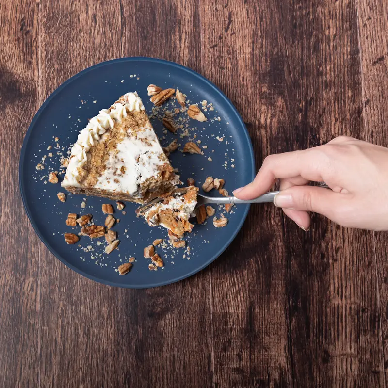 Rebanada de pastel de zanahoria con betún tomada con cuchara sobre plato azul y mesa de madera