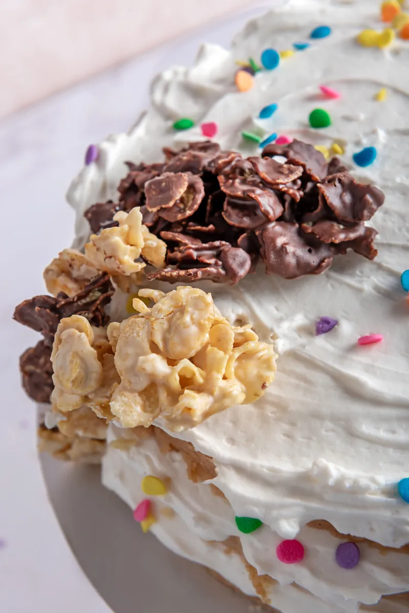 Detalle macro de pastel decorado con crema batida, confeti y toppings de chocolate y cereal